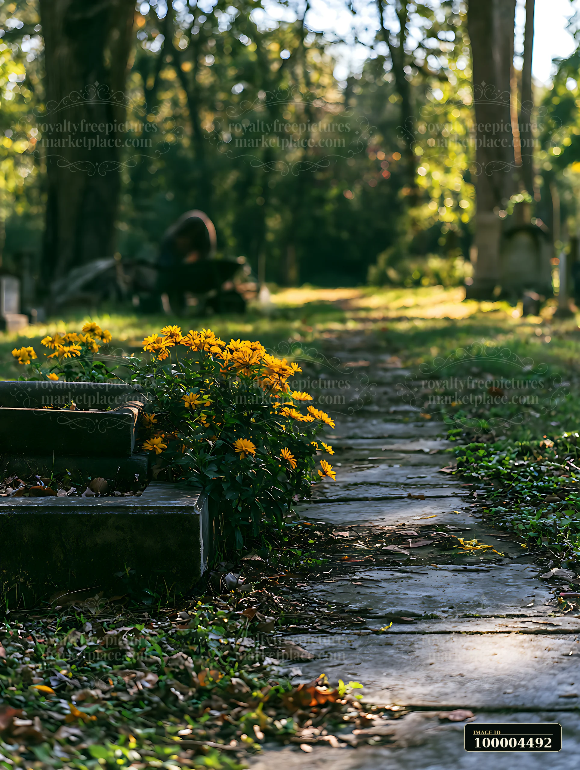 A grave with yellow flowers is situated next to a stone path in a cemetery.