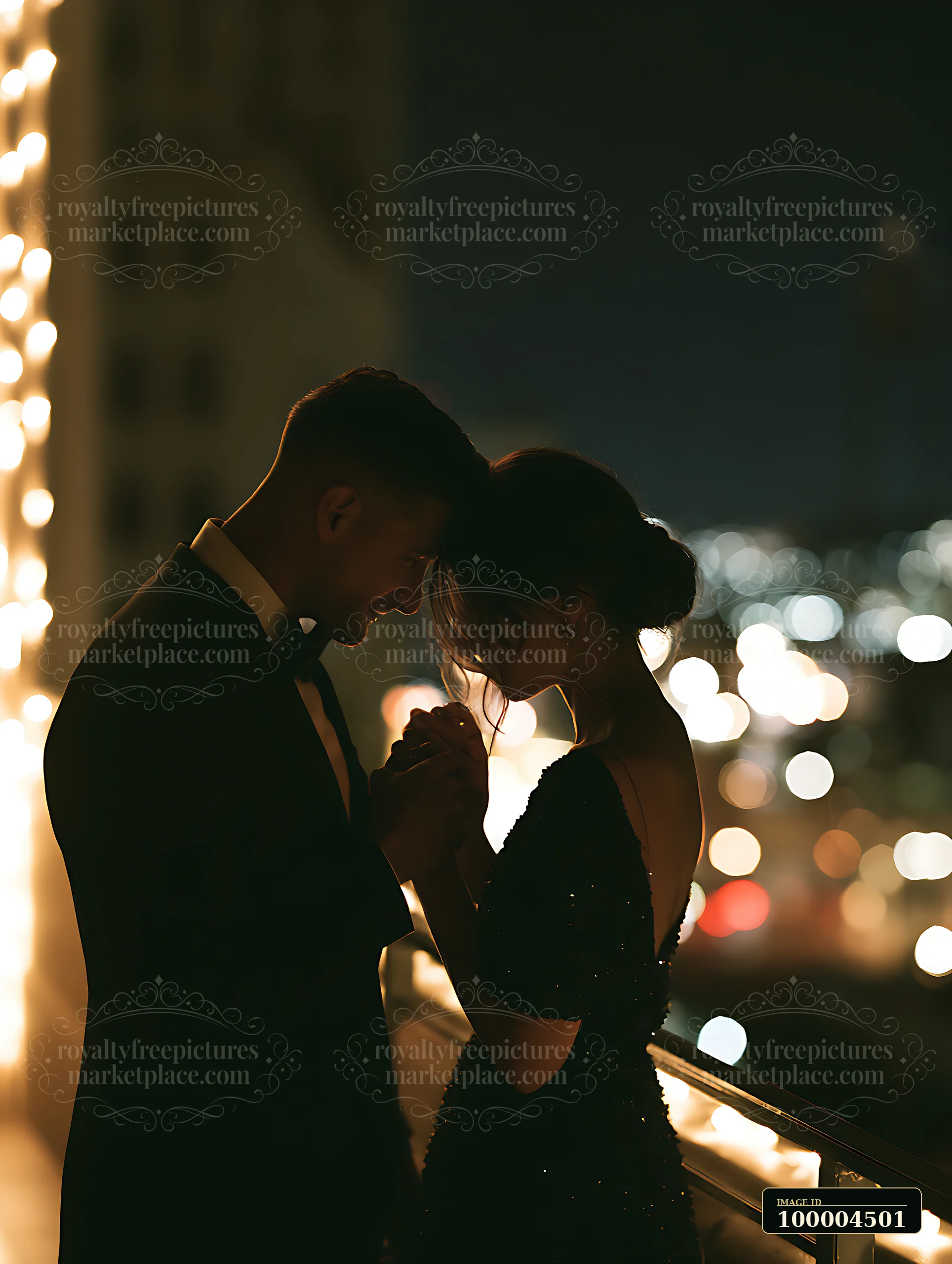 Man gently kisses a woman's hand beside a railing amid warm evening lights and blurred bokeh.
