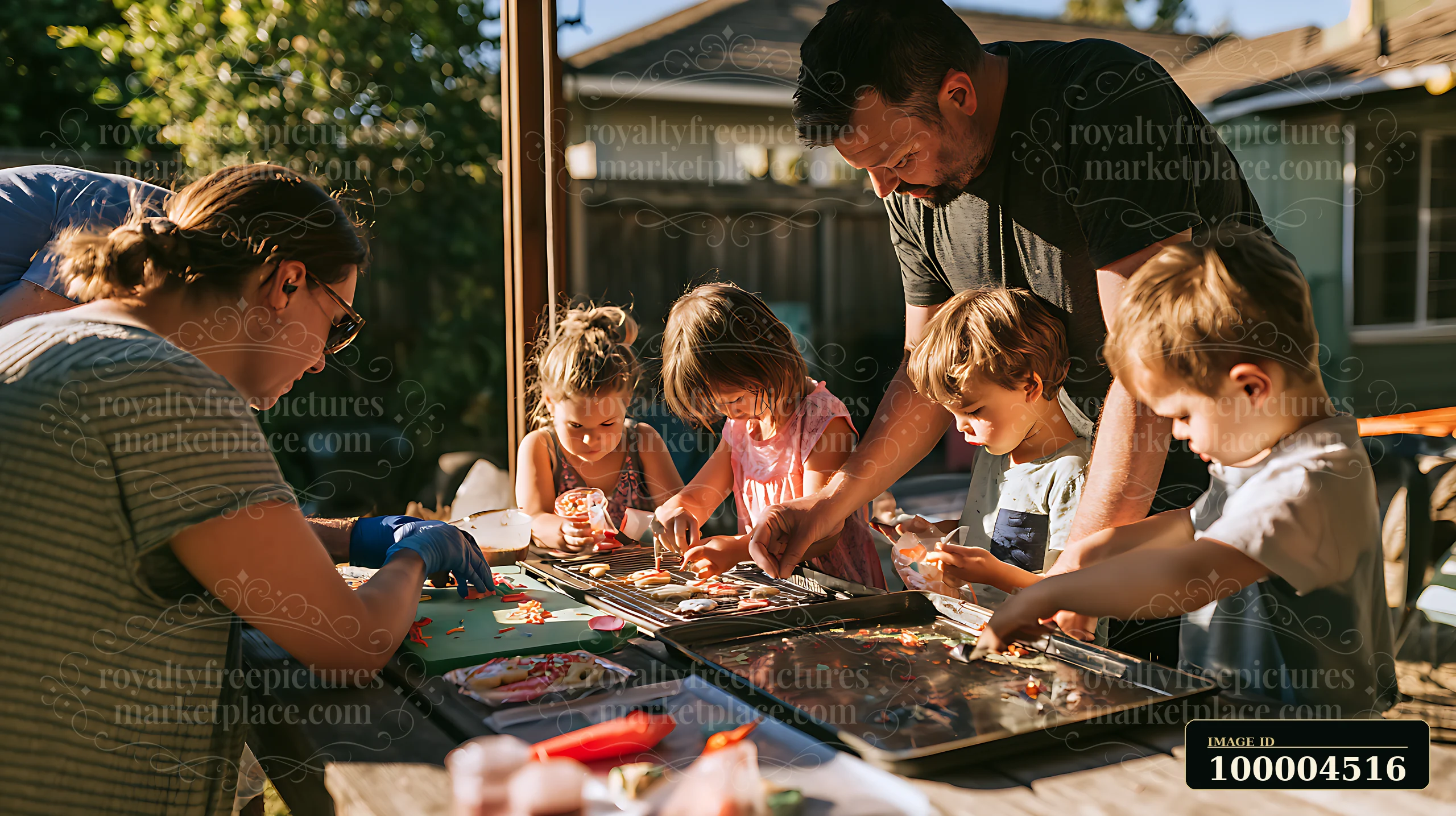 Parents helping children decorate cookies outside in a backyard on a sunny day.