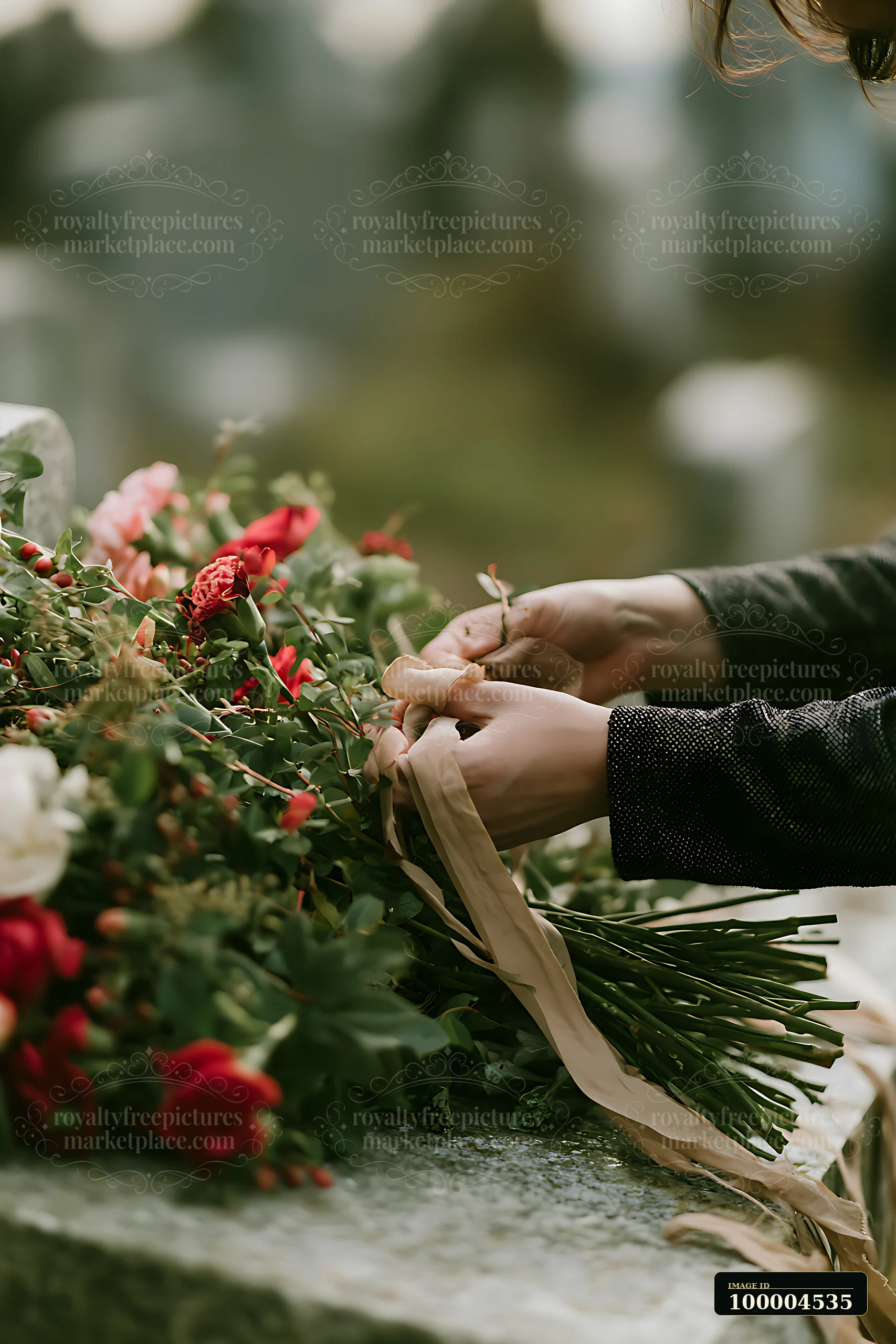 Person arranging a bouquet of fresh flowers on a grave in a softly blurred cemetery setting.