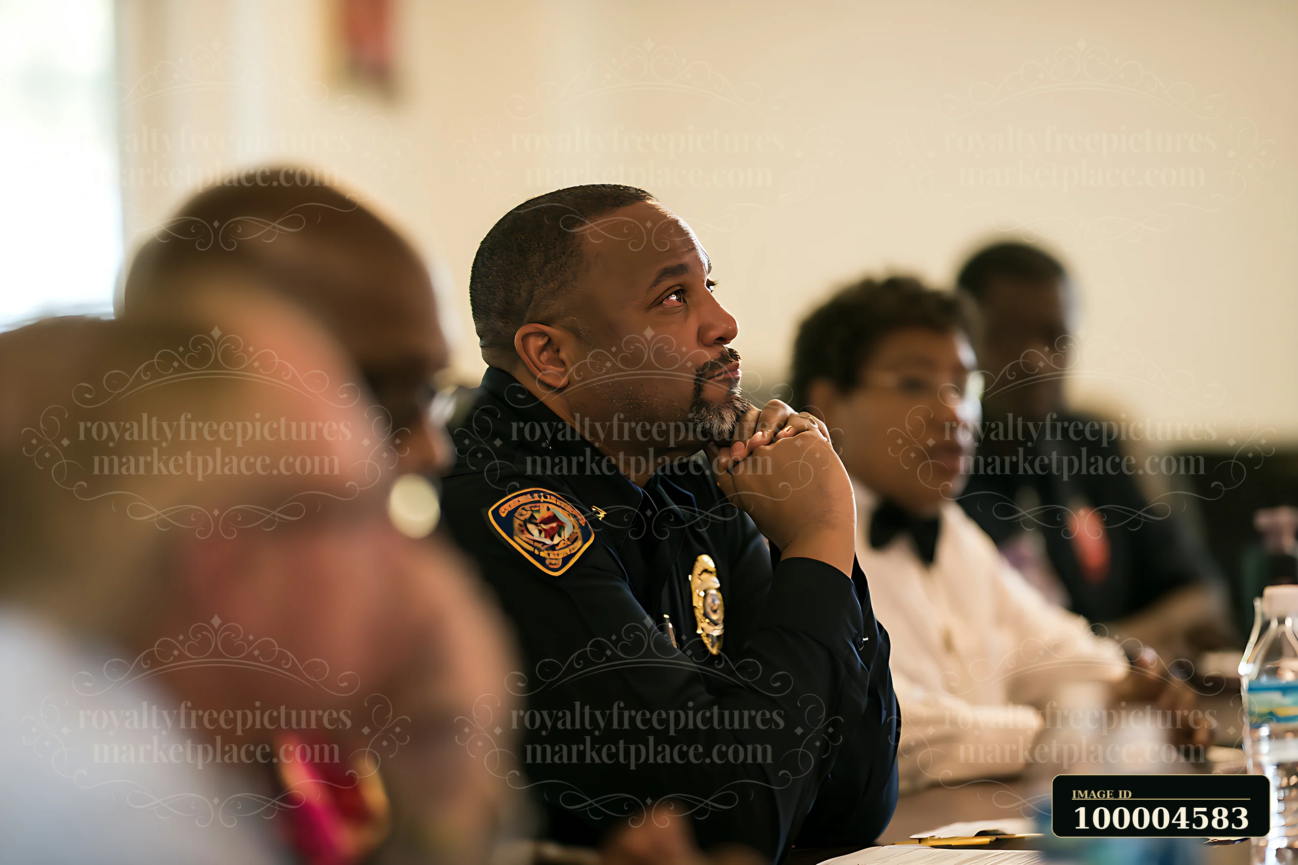 Police officer listens attentively at a seated indoor community meeting with other attendees.