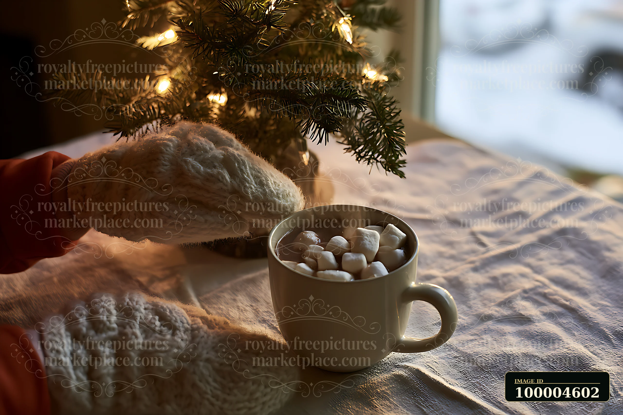 Mug of cocoa topped with marshmallows beside a decorated evergreen tree and a person in a sweater.
