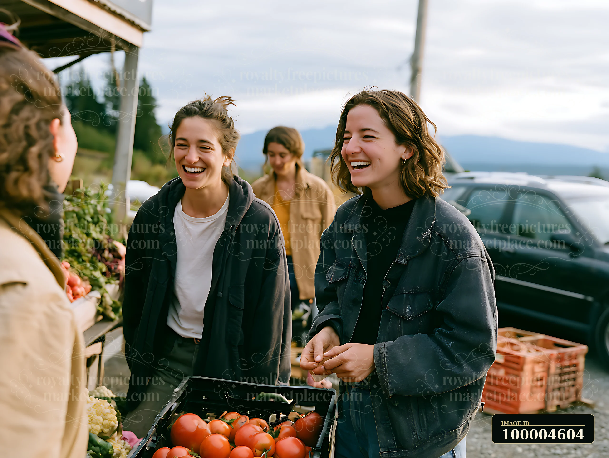 Two women smile and laugh while shopping for vegetables at a roadside market.
