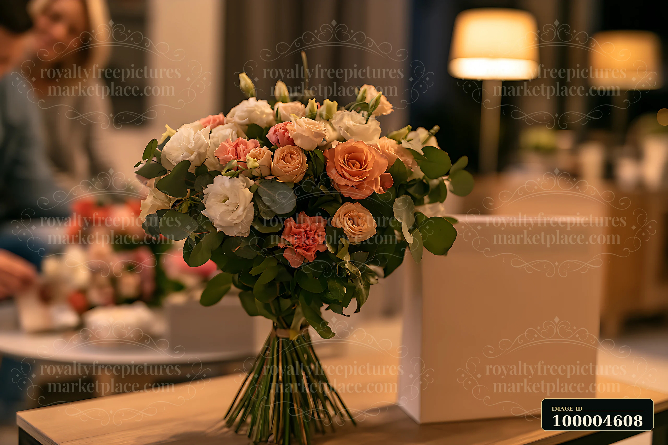 A bouquet of mixed flowers stands beside a blank gift bag on a table in a cozy indoor setting.