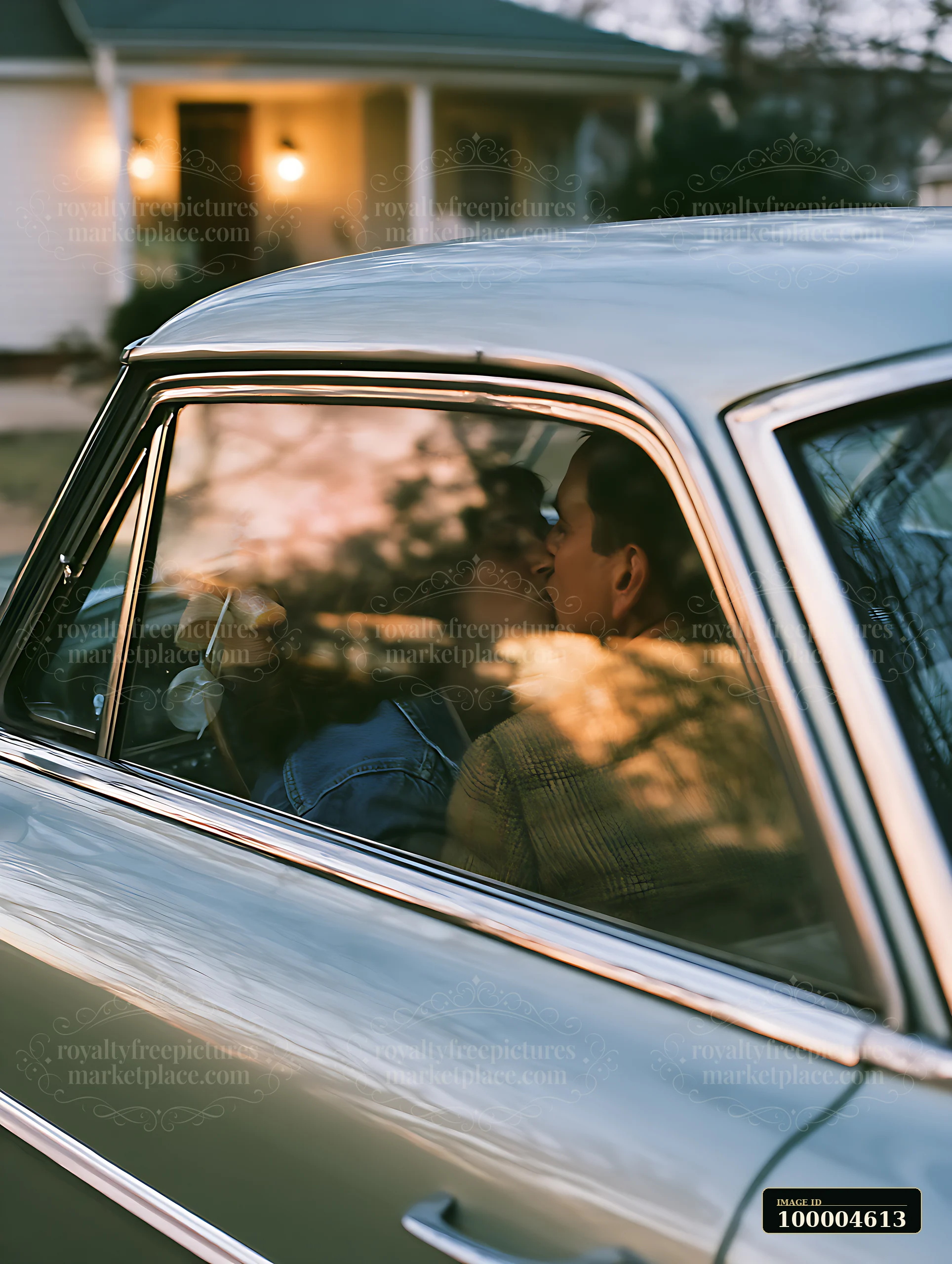 A couple is kissing inside a vintage car as the sun sets, with warm light reflecting in the car windows.
