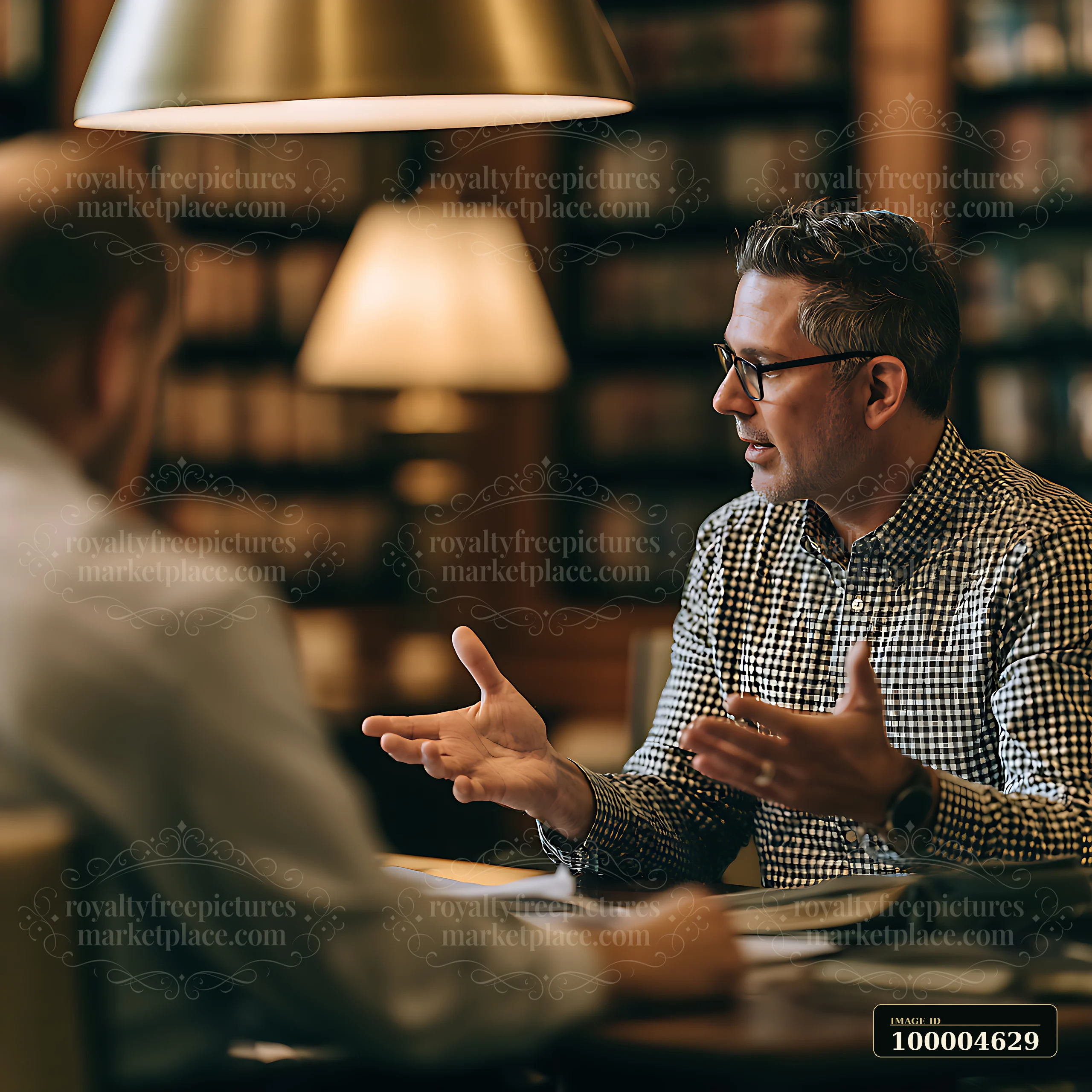 Businessman gestures while discussing documents with an advisor across a table in a warmly lit interior.