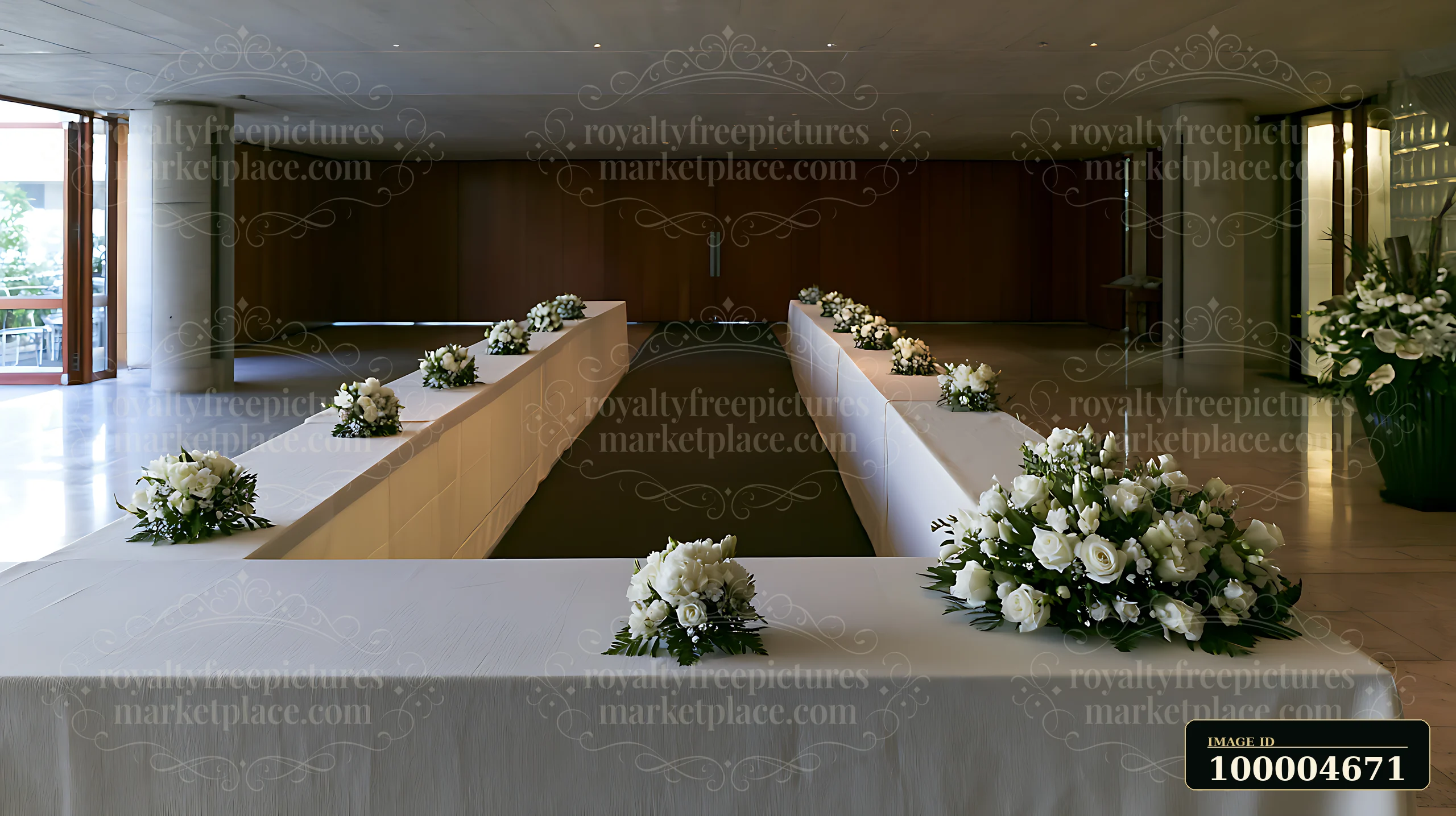 White funeral flowers arranged along plain tables in a quiet indoor hall.