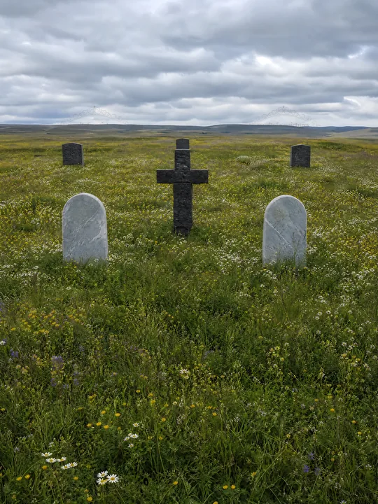 Dark Christian cross in summer meadow with gravestones - AI-generated stock image