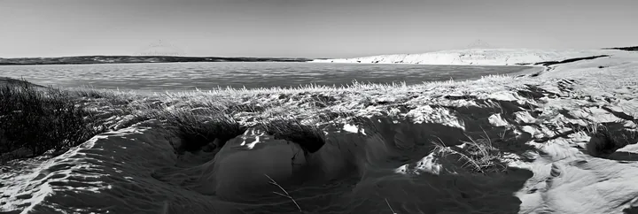Snowy lakeside meadow with frozen water in winter - AI-generated stock image