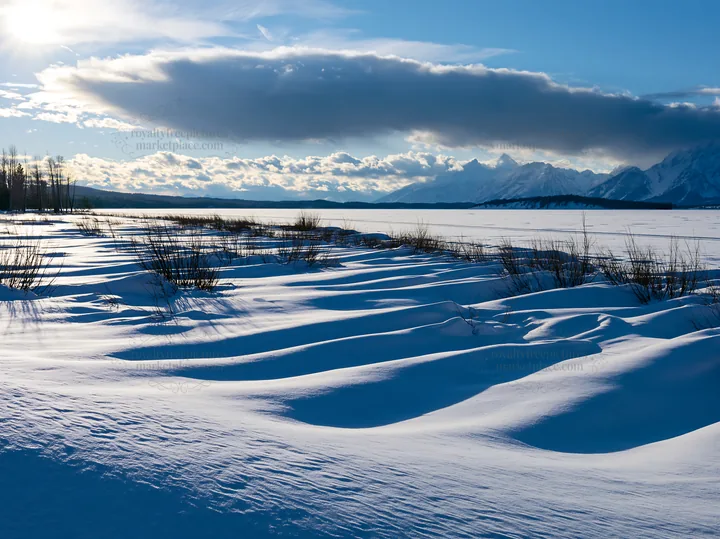 Snowy lakeside meadow with gentle snow drifts and mountains - AI-generated stock image