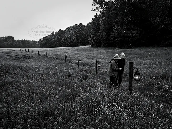 Lanterns along a meadow path at dusk with two people - AI-generated stock image