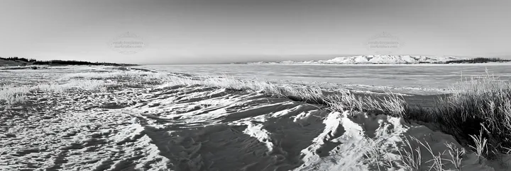 Snowy lakeside meadow with frozen water and distant hills - AI-generated stock image