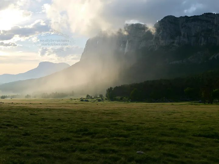 Meadow under crags with mist in the evening light - AI-generated stock image