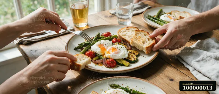 Poached eggs, grilled vegetables, tomatoes, and toast sit on a breakfast plate as people serve food at a wooden table.