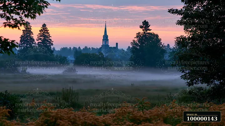 Low fog drifts across a meadow toward a church steeple beneath a pink and orange dawn sky.