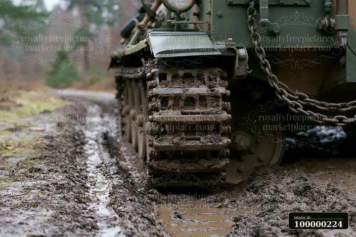 Muddy armored vehicle tracks fill the foreground on a wet, rutted forest trail.
