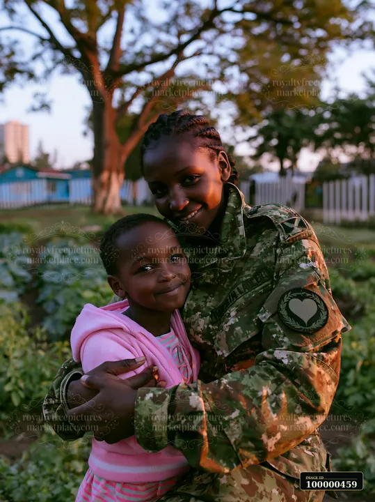 A soldier in uniform hugs a young girl while surrounded by plants in a garden during sunset.