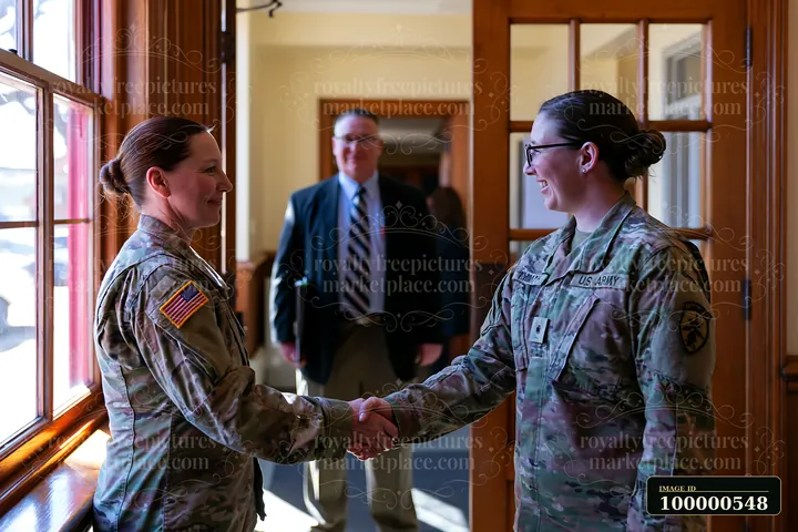 Two military personnel shake hands in a corridor.