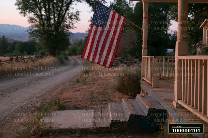 The American flag hangs from a porch on a rural road at sunset.