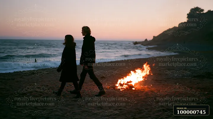 Two individuals walk along a sandy beach at sunset, with waves crashing nearby and a fire burning on the sand.