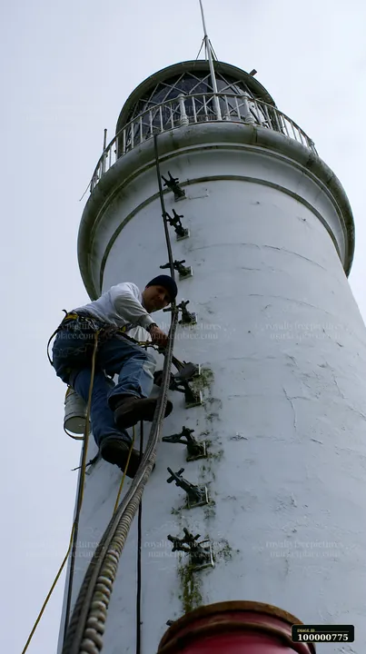 A lighthouse maintenance worker at work climbs the side of a tall lighthouse, focusing on repairs.