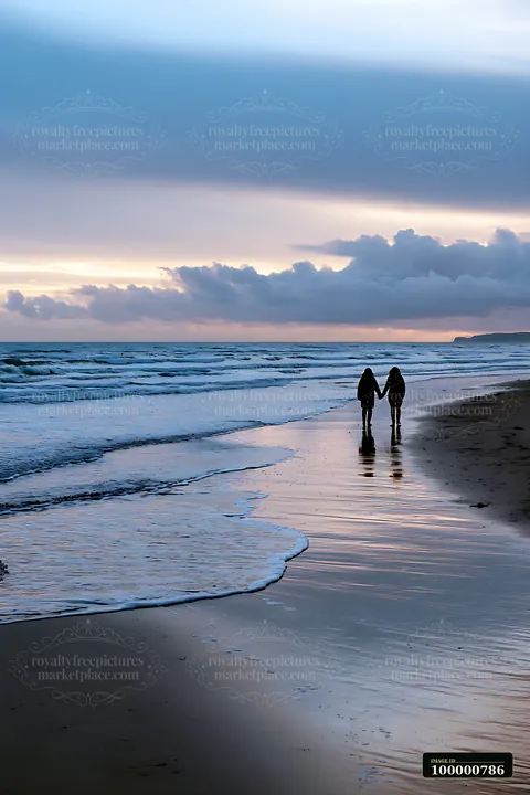 A couple walks hand in hand along the shore as waves gently lap at the sand.
