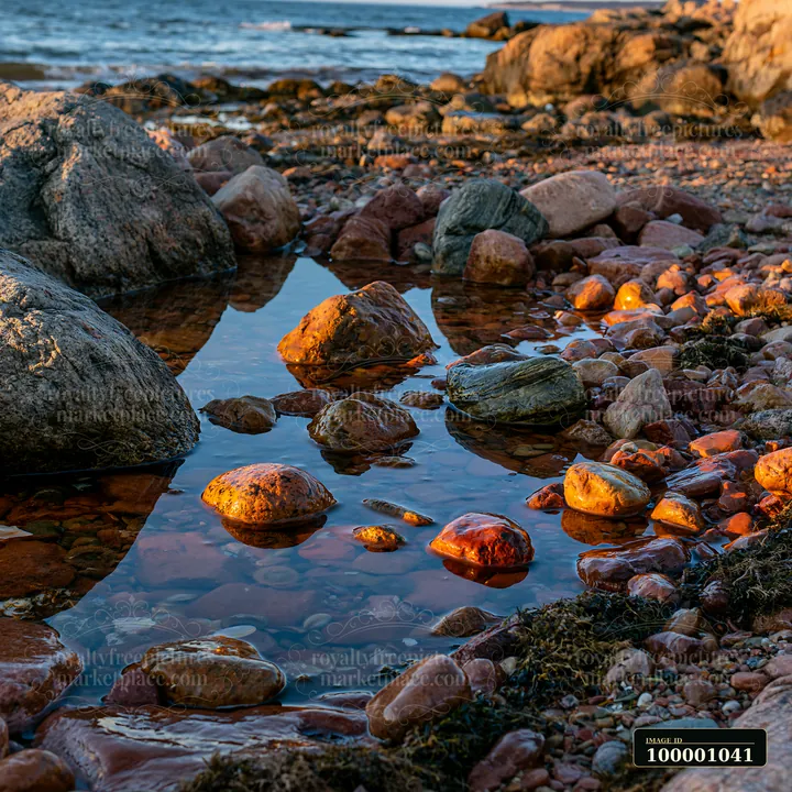 Rock formations and pebbles are visible along the coastline with exposed rocks at low tide.