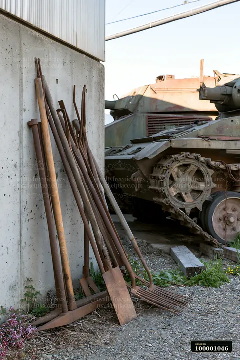 Rusty tools for maintaining a panzer tank rest against a wall next to the vehicle.