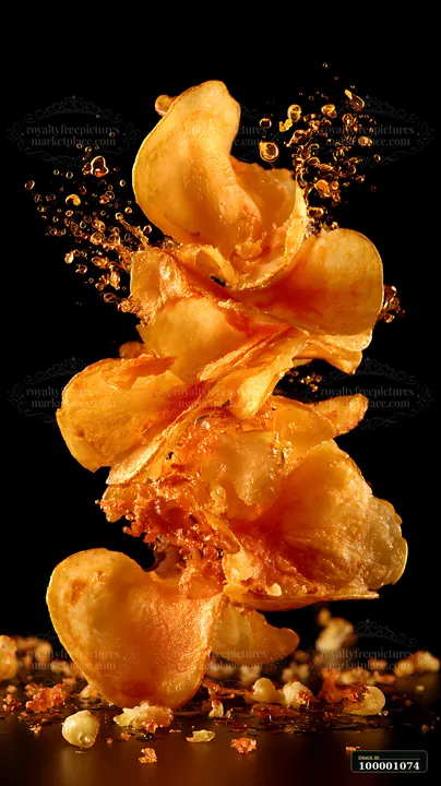 A stack of golden crispy potato chips is suspended in the air with crumbs scattering around it against a dark background, showcasing a flavorful and crunchy sna