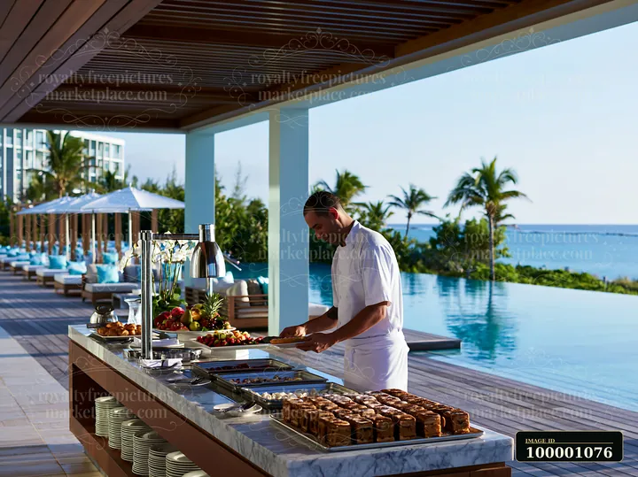 A chef prepares dishes at a poolside buffet table beside an infinity pool and palm trees, providing fresh food options for guests enjoying the sunny day outdoor