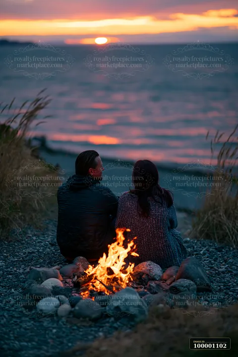 A couple enjoys a bonfire on the beach as the sun sets over the coastline with beach bonfire.