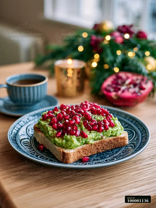 This breakfast plate features avocado toast topped with pomegranate seeds, next to a cup of coffee, with warm light from nearby decorations and greenery in a co