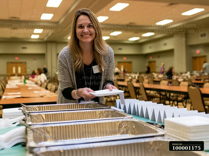 A server organizes plates at a catering buffet setup in a spacious hall.