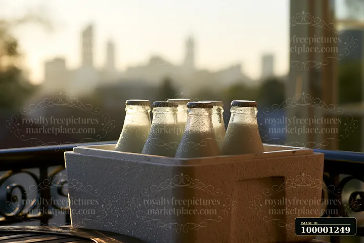 Milk bottles in an insulated delivery box sit on a balcony with a city skyline background.