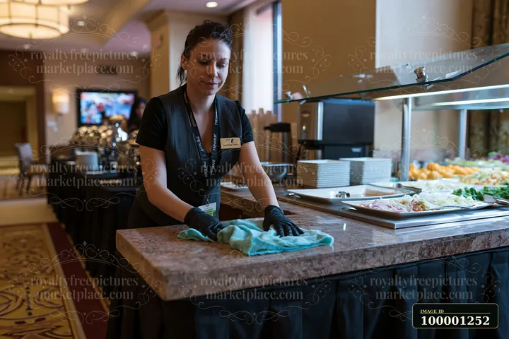 A catering staff member is cleaning a buffet table in a conference setting.