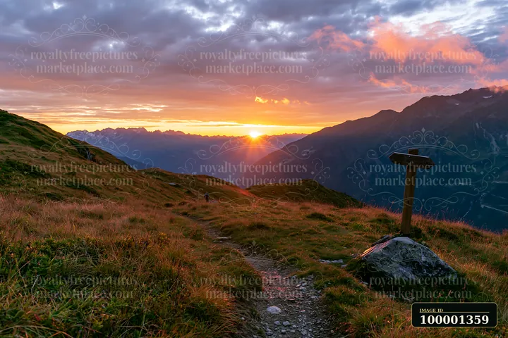 A vibrant sunset illuminates the Swiss landscape in golden light, with a winding hiking path, green grass, and distant mountains creating a beautiful scene.