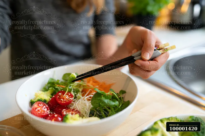 A person with limited hand mobility using utensils works on eating a fresh salad in a kitchen.
