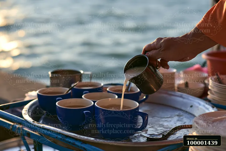 A street food vendor adds milk to a cup of tea at a market near the waterfront.