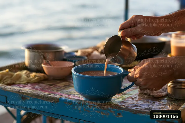 A street food vendor adding milk to tea at a busy food stall by the water.