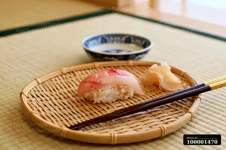 One sushi piece with pickled ginger is placed on a bamboo plate.