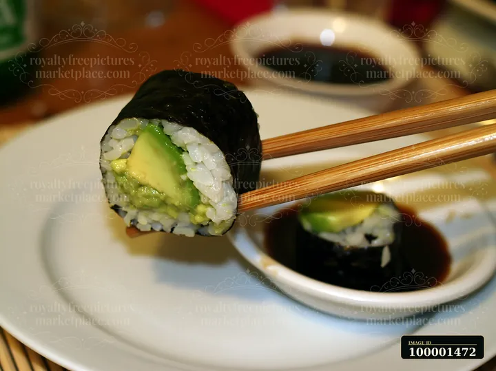 A single sushi piece is held with chopsticks above a plate.