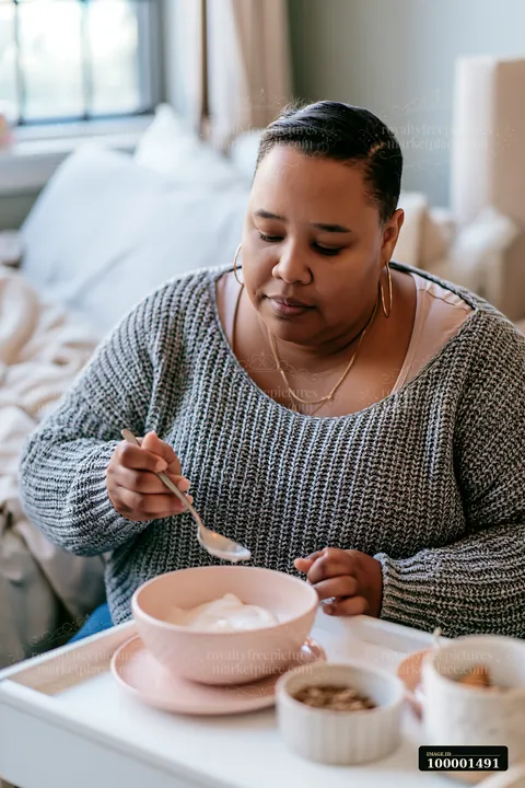 A person with limited hand mobility using utensils sits at a table eating breakfast in a cozy home setting.