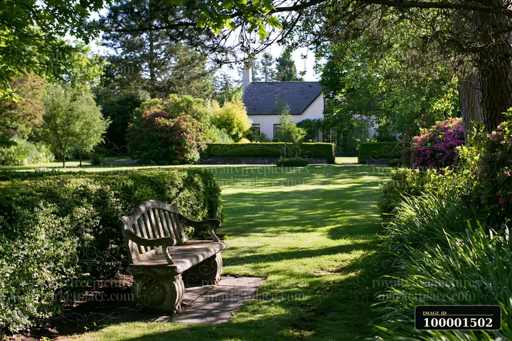 A country house surrounded by hedges sits in a green garden with trees and flower bushes.