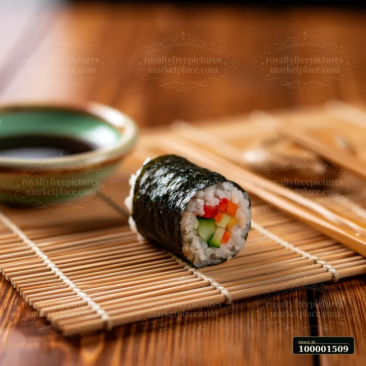A single sushi roll on bamboo mat sits beside a small dish of soy sauce and chopsticks.
