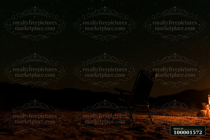 A chair sits near a fire pit in a desert campsite under a starry night sky.