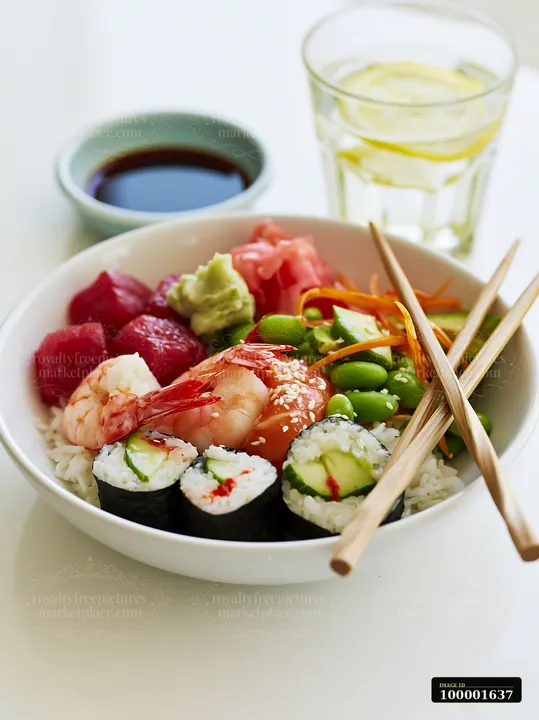 A bowl contains sushi, shrimp, fish, vegetables, and rice, with chopsticks resting on the side.
