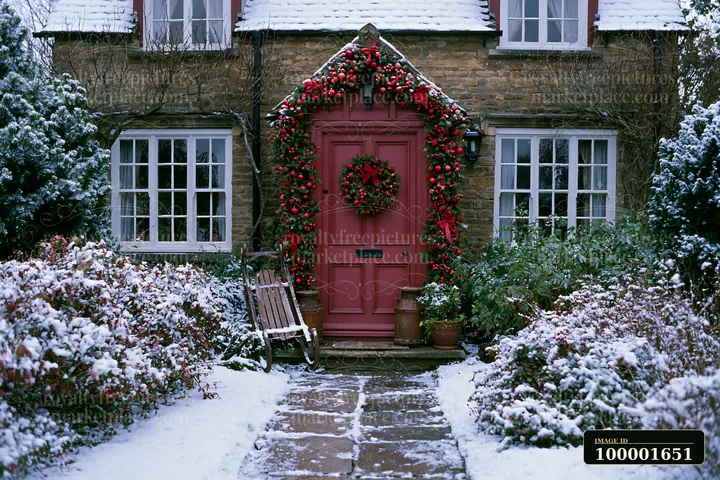 Snow covers the ground around a country cottage with Christmas decorations.