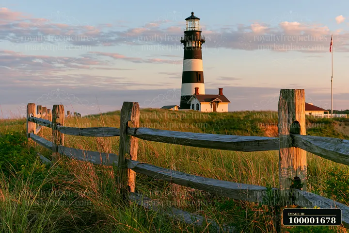 A lighthouse with black and white stripes stands tall beside a wooden fence.
