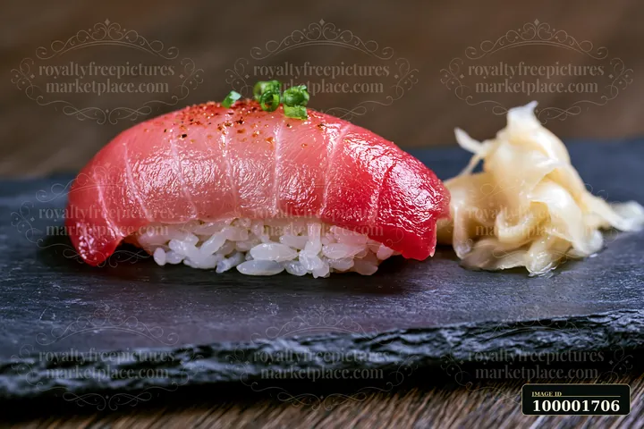 One sushi piece with pickled ginger sits on a black stone plate.