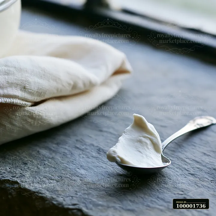 A spoon holds a small amount of cream placed near a cream-colored fabric.